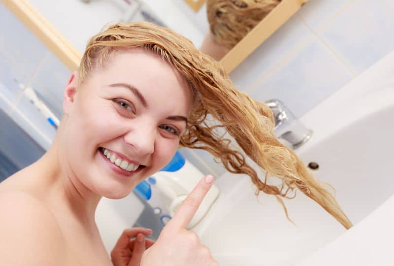How Damaging Is A Bleach Bath For Hair? Here's The Truth. 2 does a bleach bath damage hair - lady doing a bleach bath with wet blonde hair over a sink