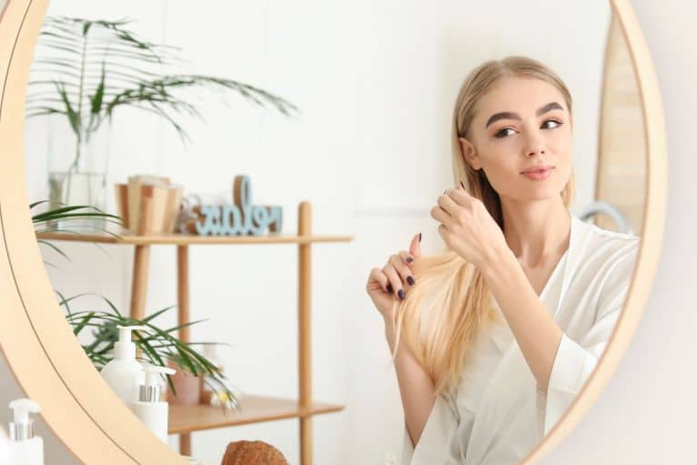How To Bleach Hair Safely At Home | The Easy Guide For Beginners. 7 young blonde woman looking in the mirror is pleased with her home bleaching