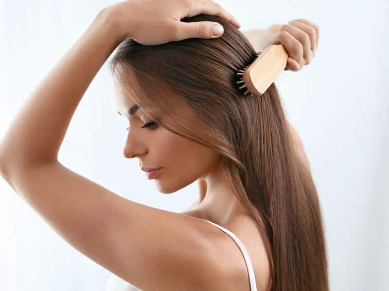Show a vibrant, shiny head of hair being brushed or styled, with a focus on the use of protective sprays or nourishing treatments to restore hair’s natural luster.