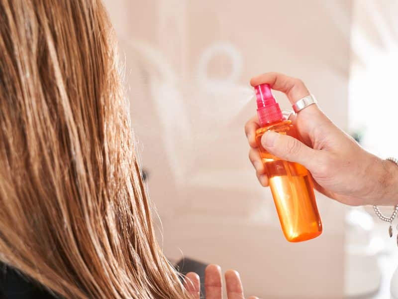 woman spraying her hair with DIY spray from a bottle